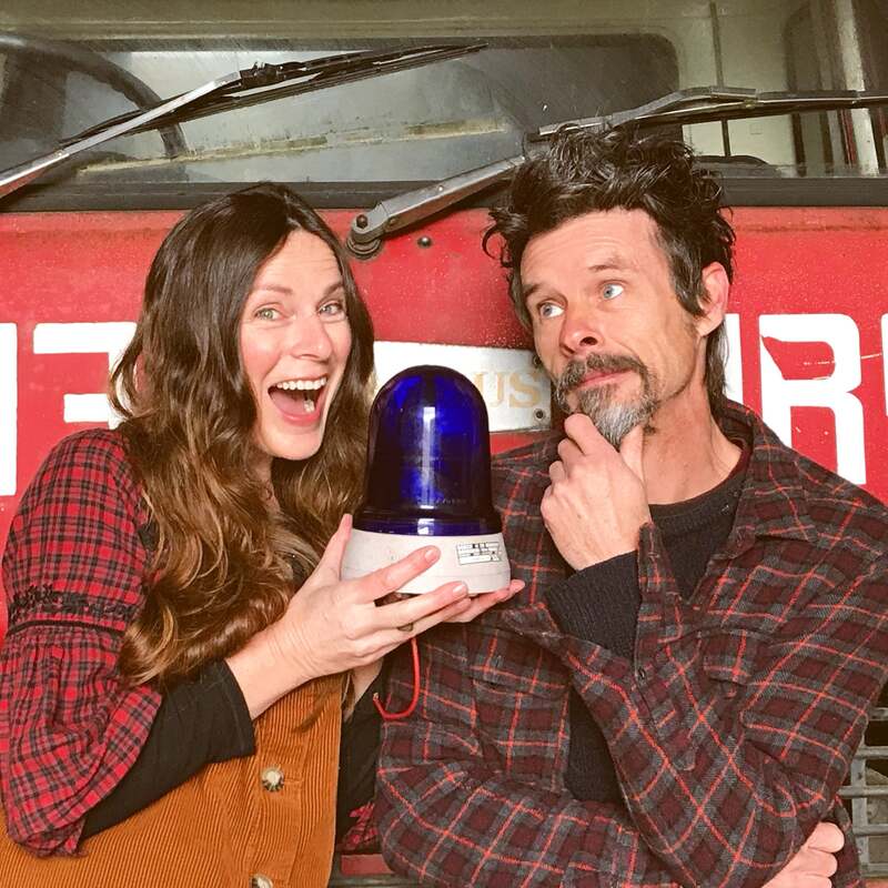 Close up of man and woman with a blue light standing in front of a vintage Bedford fire engine