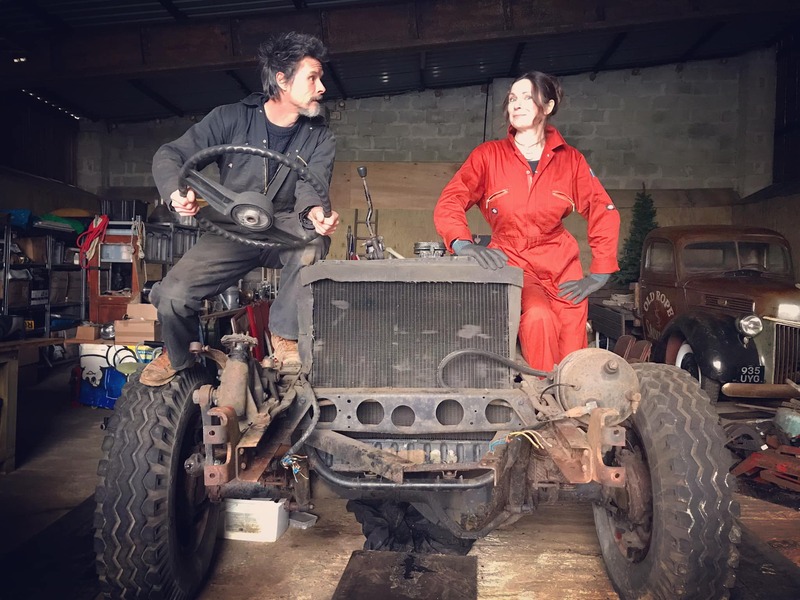 Man and woman pretending to drive the disassembled chassis of an old Bedford truck