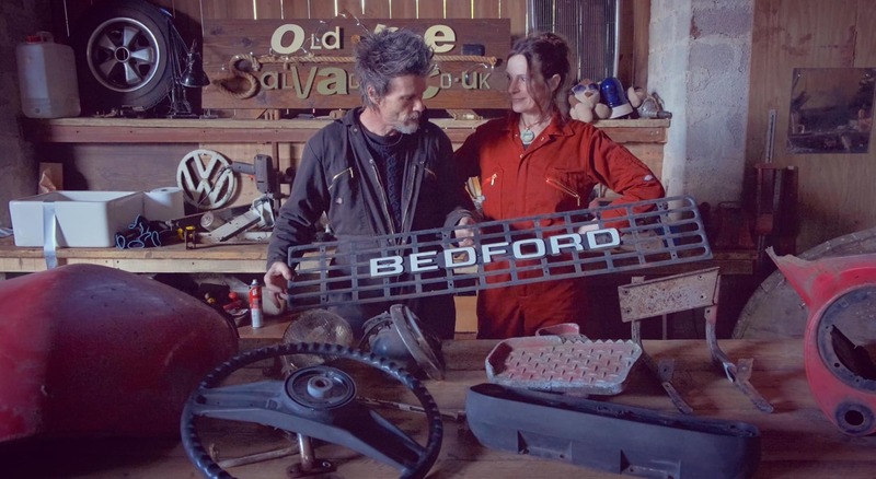Man and woman standing at a workbench with some old Bedford truck parts