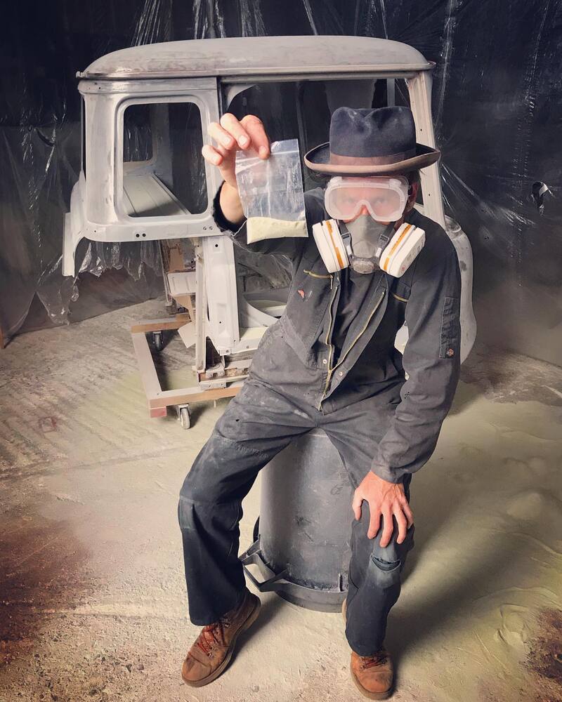 Man in goggles and mask with a Bedford truck cab he is sandblasting