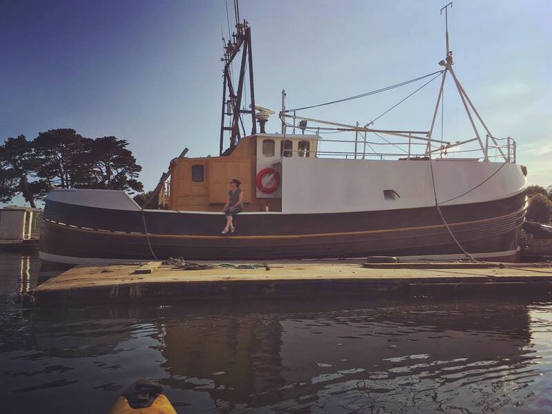 Woman sitting on the side of a large old wooden boat in harbour
