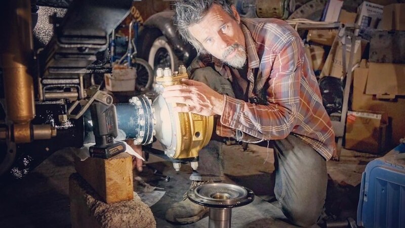 Man crouching next to a newly restored Bedford truck axle