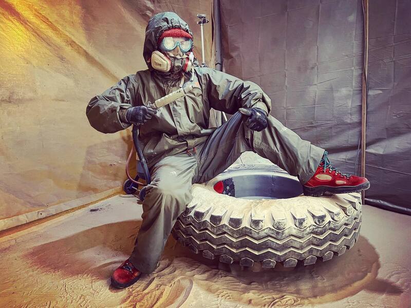 Woman in protective clothing sitting on a tyre with a sandblaster in hand