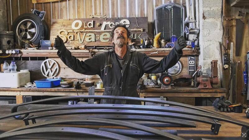 Man in black overalls at a workbench with arms in air looking happy