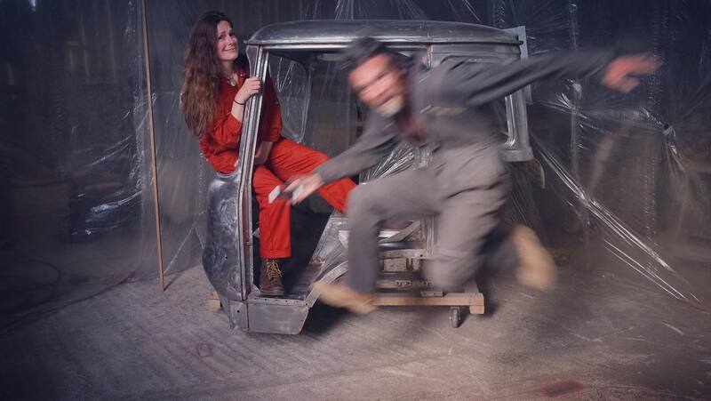 Man and woman in the shell of a Bedford Truck cab in bare metal