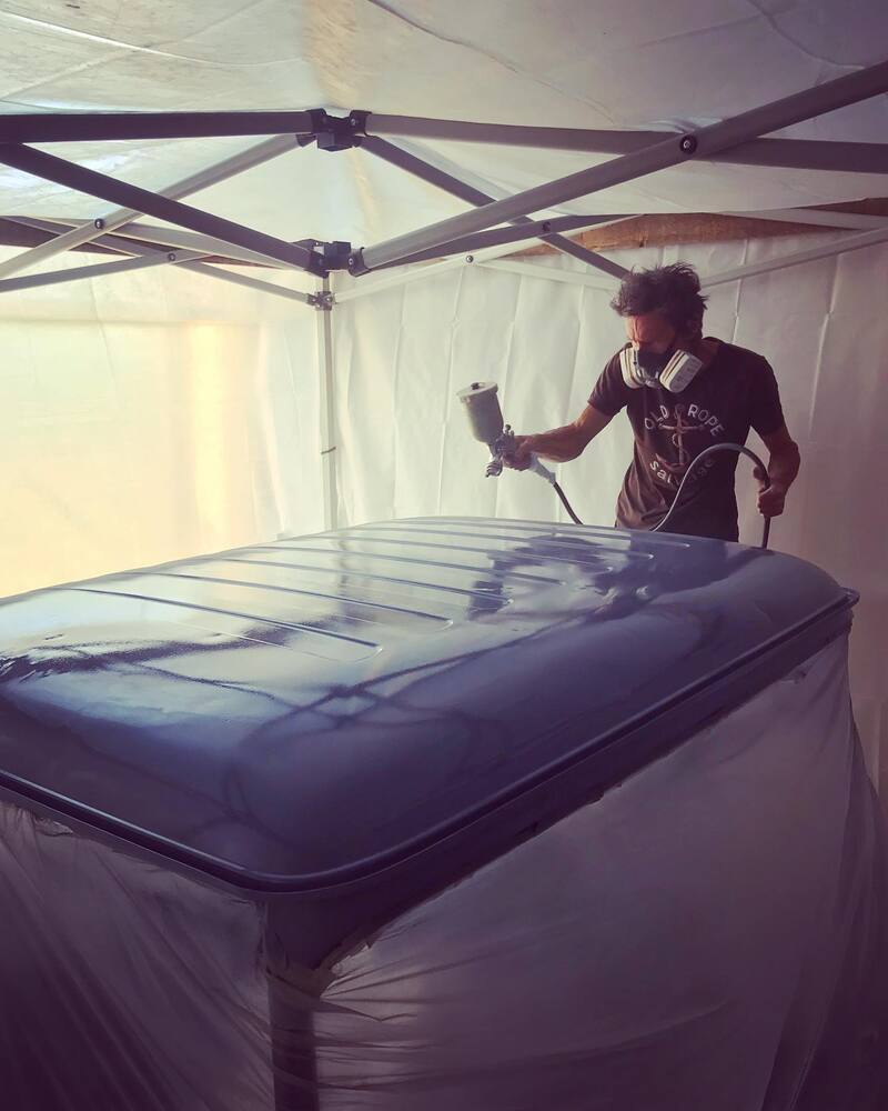 Man spray painting a Bedford truck cab in grey primer