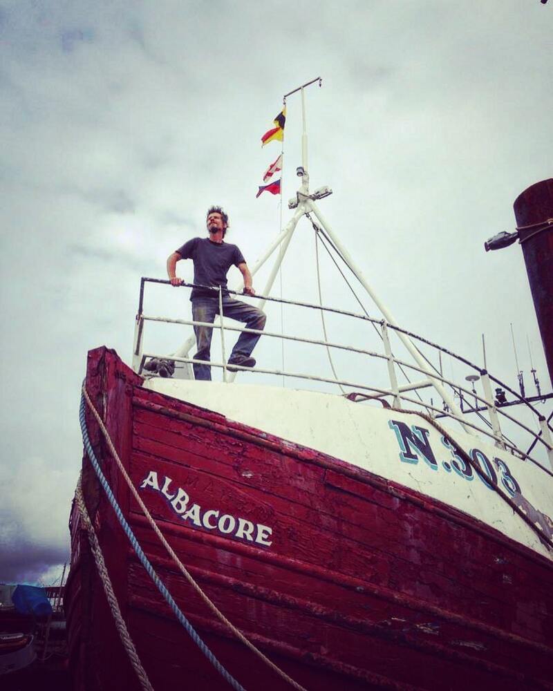 Man standing on top of an old red painted fishing trawler fishing boat