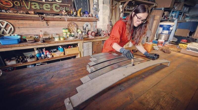 Woman in orange overalls at a workbench painting owetrol oil on to leaf springs