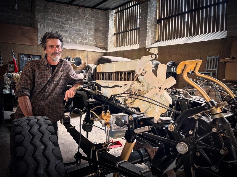 Man standing next to the newly restored chassis and white painted engine of a classic Bedford truck