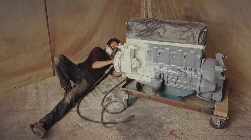 Man lying on floor painting a petrol truck engine white