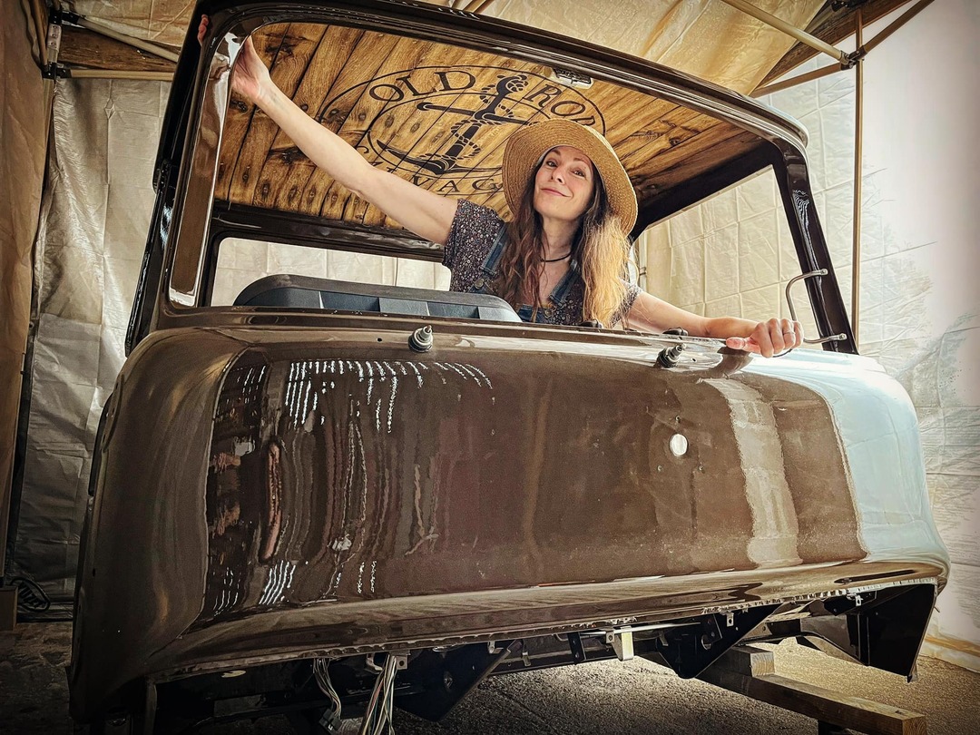 Woman in a straw hat sitting inside the cab shell of a Bedford truck
