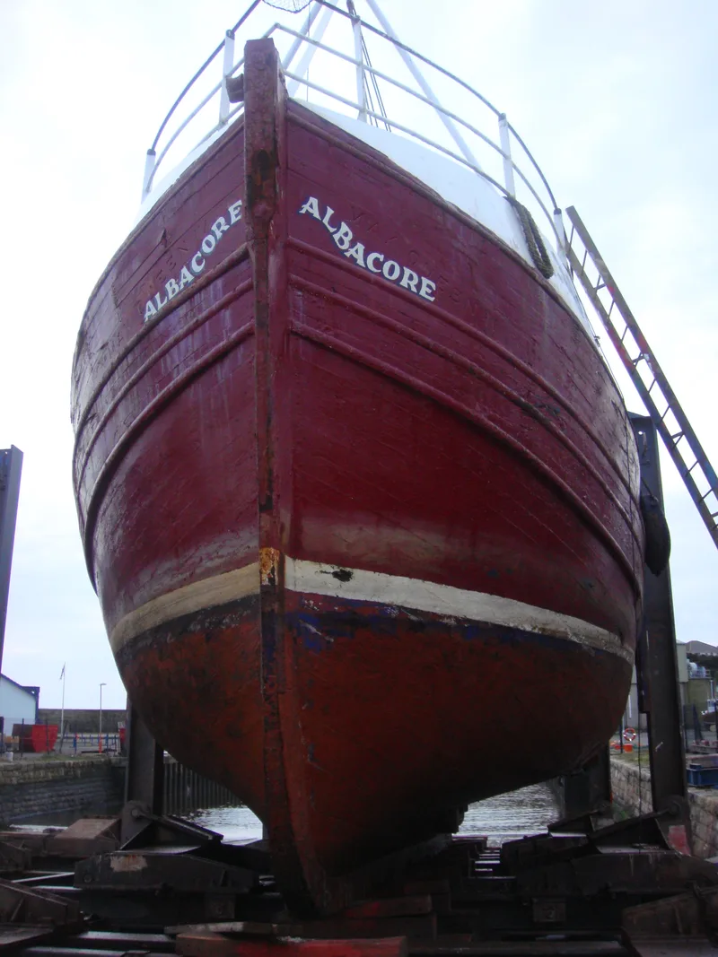 Front view of old red and white wooden fishing trawler Albacore standing out of the water in dry dock