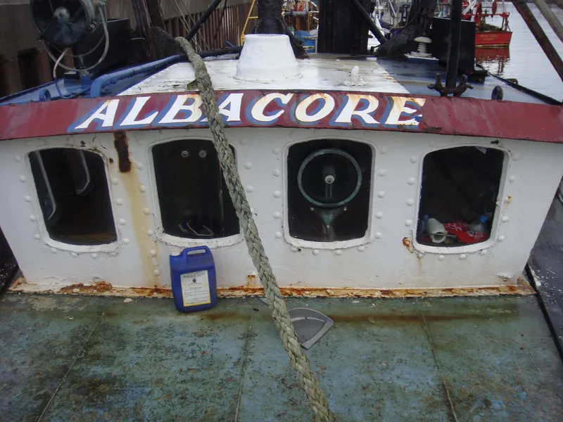 Close up view of the windows of the wheelhouse of an old fishing trawler with the name Albacore in white lettering