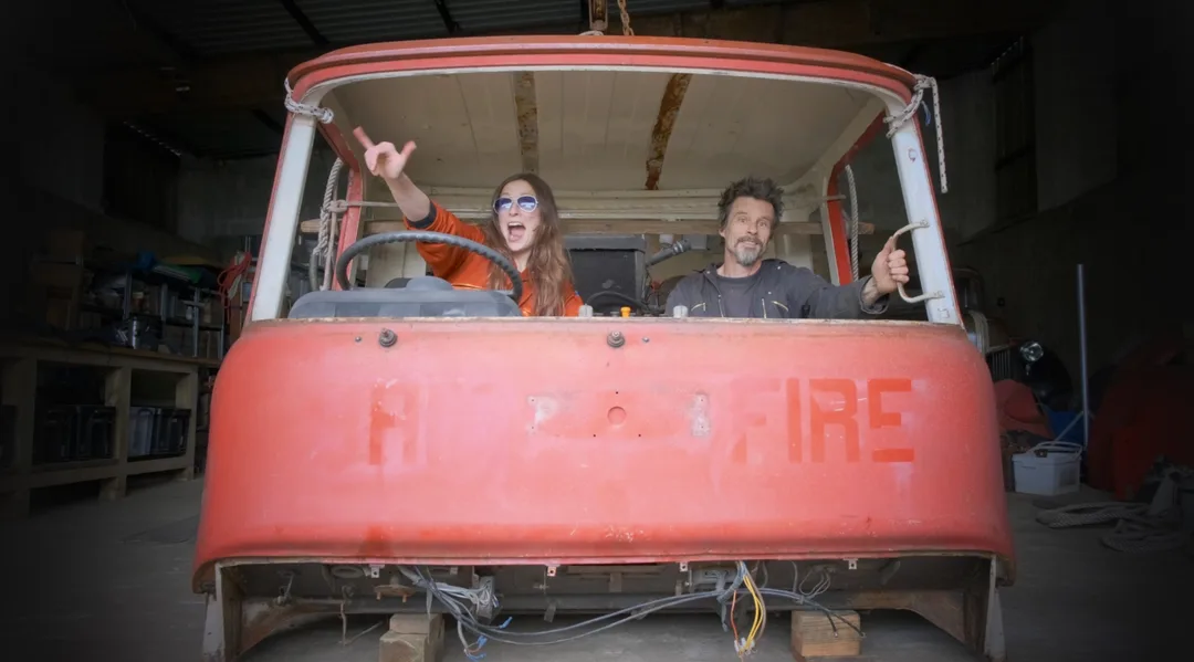 Man and woman in the cab of an old red Bedford fire truck