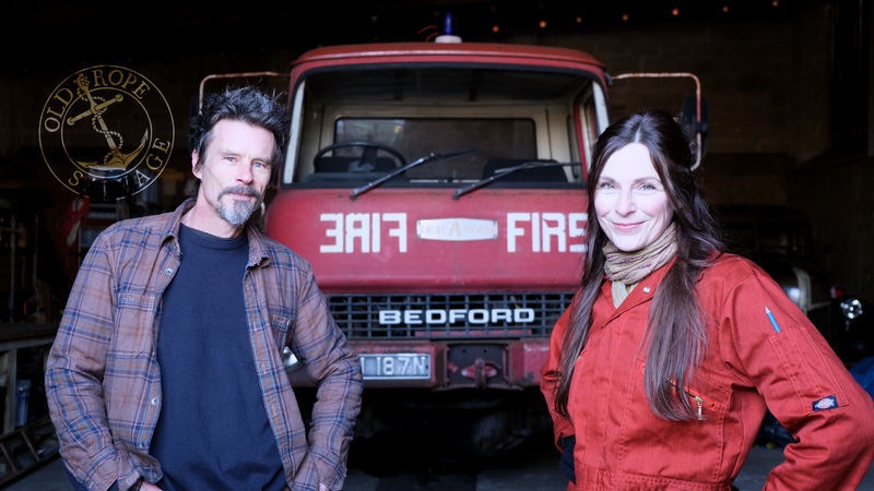 Man and woman standing in front of an old Bedford fire engine