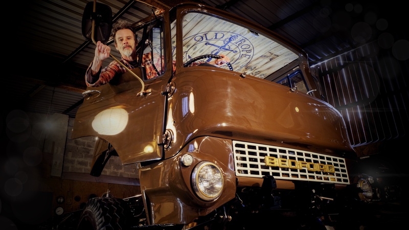 Man viewed from below sitting in the cab of a newly restored Bedford truck painted in brown