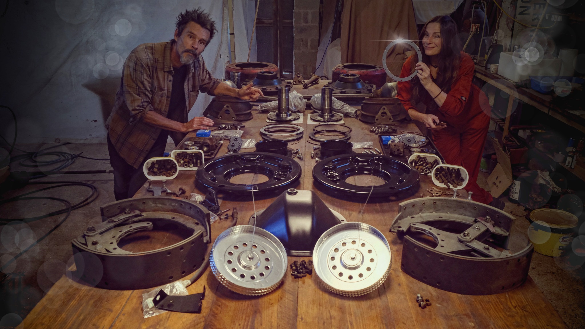 Man and woman standing at a workbench with the parts of a truck axle dismantled in front of them
