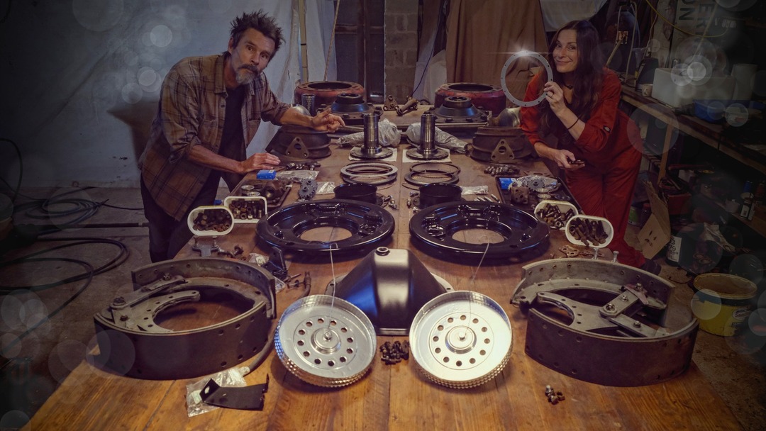 Man and woman standing at a workbench with the parts of a truck axle dismantled in front of them

