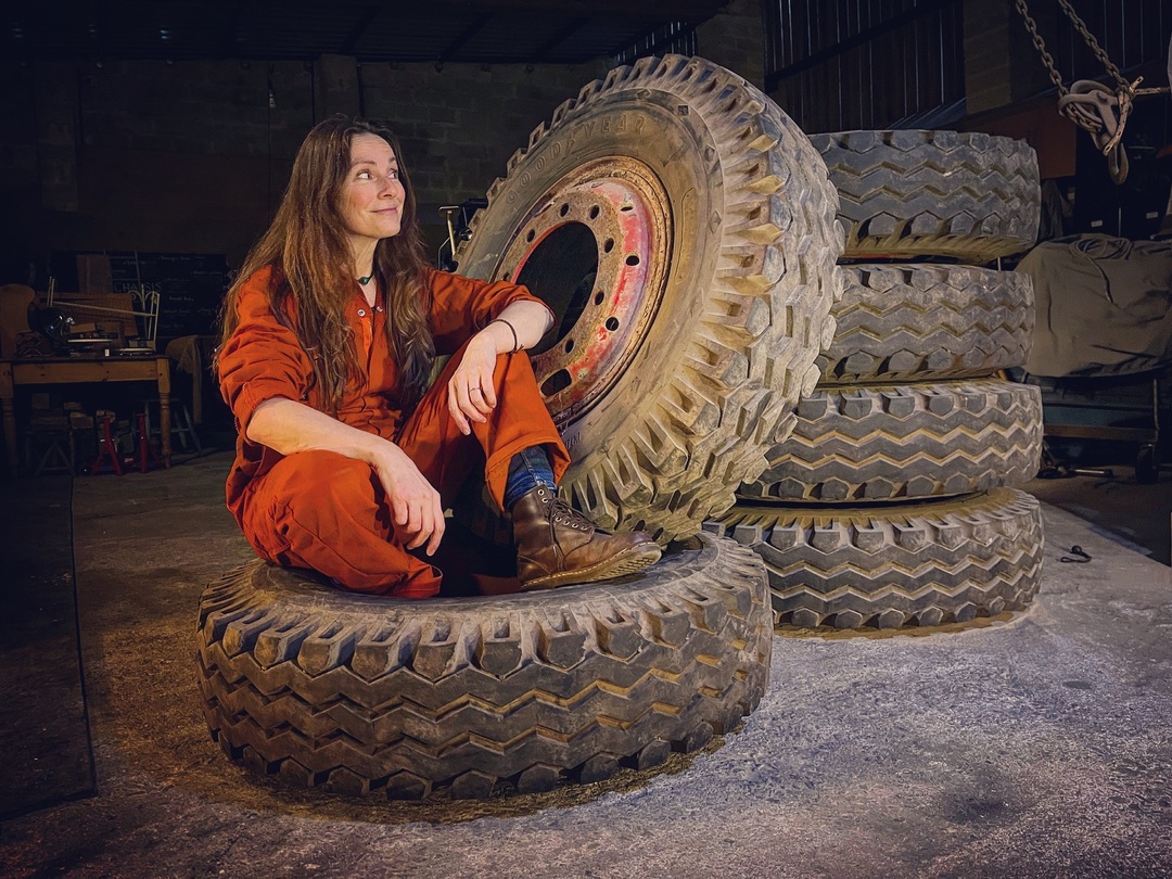 Woman in orange overalls sitting on a pile of truck tyres